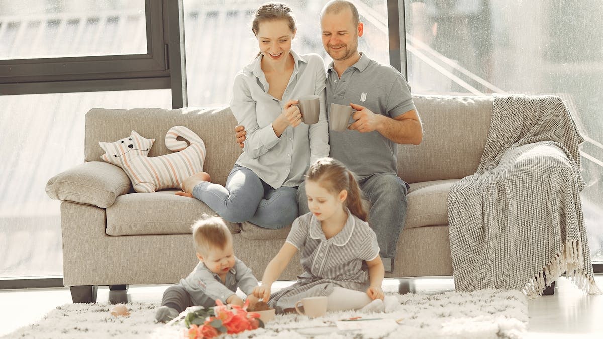 Cheerful family wearing casual clothes sitting in living room while playing and drinking tea during weekend at home in morning